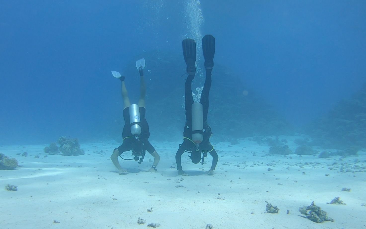 A picture of a daily diver and his guide having fun by doing a handstand underwater on the sea floor.